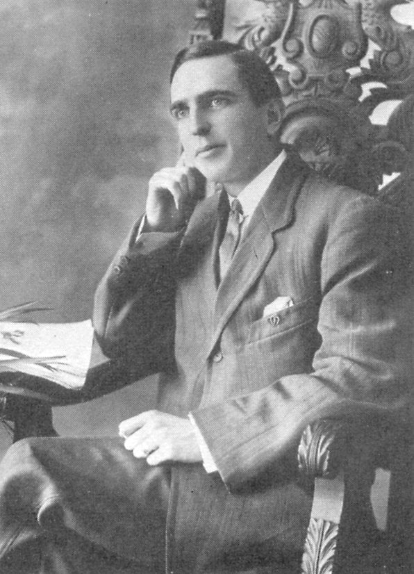 Black and white portrait of man posed at desk with one hand on chin.