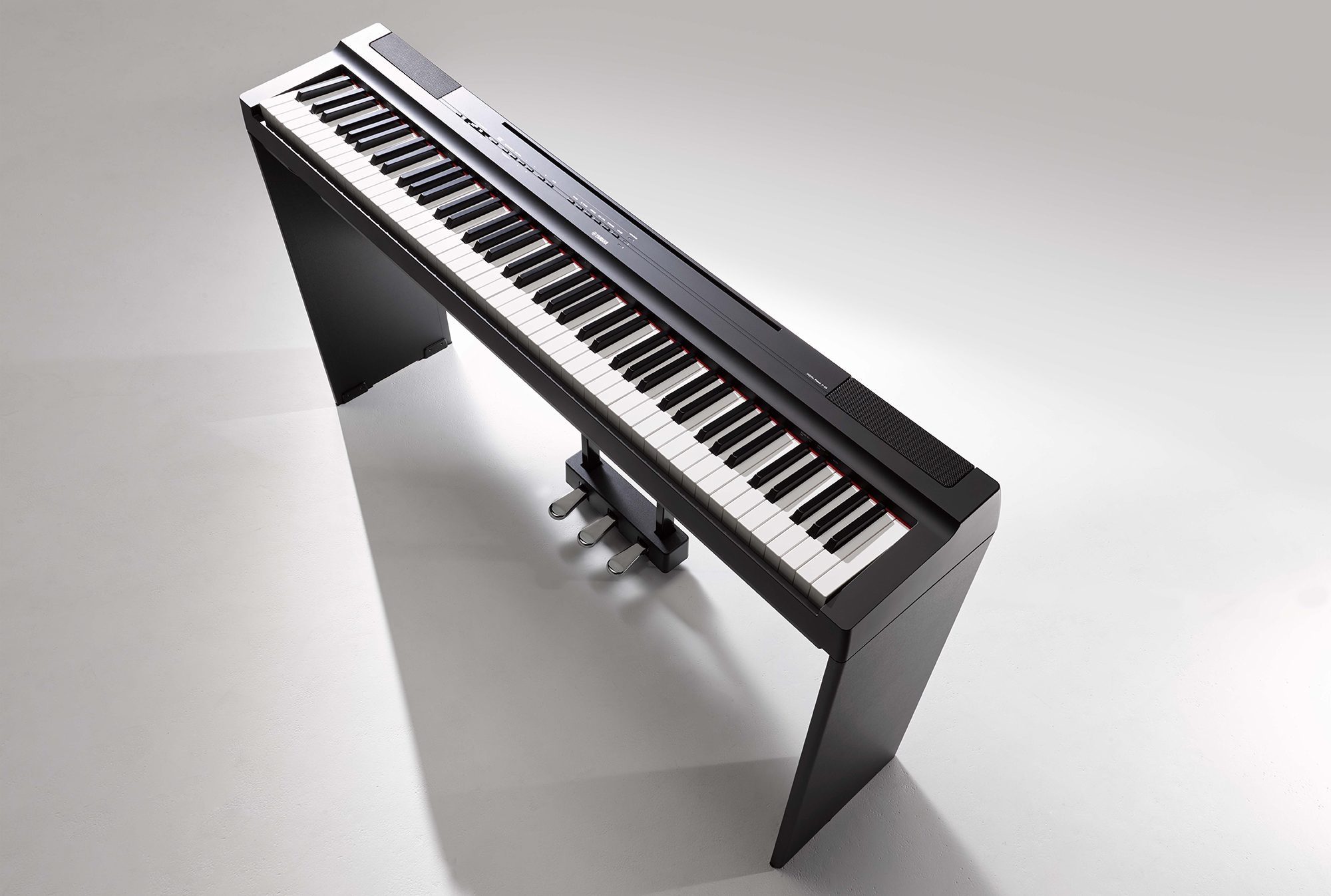 Best beginner keyboard - black keyboard with more buttons on stand with three-pedal unit, birds eye view on white background.